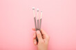 Young adult woman hand fingers holding and showing three new different makeup brushes with soft bristles on light pink table background. Pastel color. Female beauty product. Closeup. Top down view.