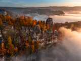 Fototapeta Londyn - Saxon, Germany - Aerial view of the Bastei on a foggy autumn morning with colorful autumn foliage and heavy fog under the rock. Bastei is a rock formation in Saxon Switzerland National Park