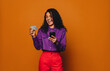 Joyful woman paying with smartphone on orange background