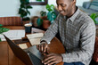 Smiling young African businessman working from home using a laptop