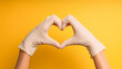 © hardvicore - Hands in white medical gloves showing heart gesture. World health day. Yellow background.