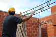 Builder lifting an iron column to make beams. Bricklayer with safety helmet and gloves working on a house under construction.