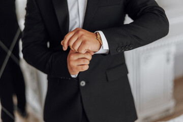 Wall Mural - A man in a suit is wearing a gold watch and adjusting his cuff. Concept of formality and attention to detail, as the man takes care to ensure his appearance is polished and professional