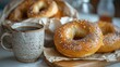 A black ceramic cup of coffee sits on a white table next to a bag of carbonated bagels that is placed in a plastic bag.