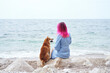 A Shiba Inu dog cozily nestles into a woman with striking pink hair, overlooking the tranquil sea. Their affectionate embrace embodies a special human-animal bond