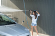 slim woman washes the foam off her car with a help high pressure water gun