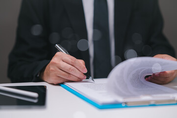 Businessman in a suit is writing with a pen on a piece of paper. Concept of professionalism and formality, as the man is dressed in a suit and tie in office. finance professional approve loan.