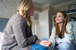Mature Mother Sitting On Bed With Teenage Daughter At Home Wearing Orthodontic Braces Talking And Laughing