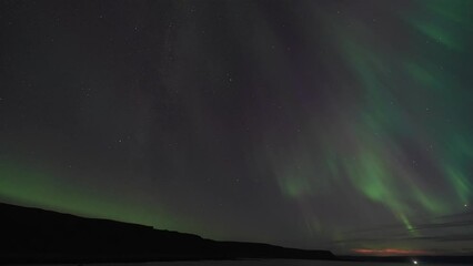 Wall Mural - The winter sky is illuminated by the beautiful dance of the Aurora Borealis over the dark still waters of the fjord.