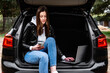 Young woman sitting in car trunk with laptop in nature.