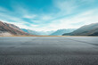 Empty asphalt under a blue sky and rolling mountains in the distance