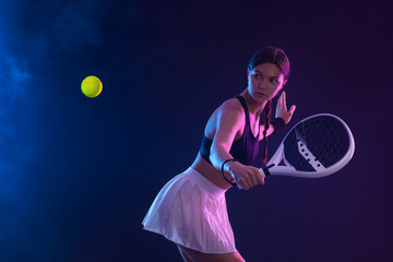 Padel tennis player with racket on tournament. Girl athlete with paddle racket on court with neon colors. Sport concept. Download a high quality photo for design of a sports app or tour events.