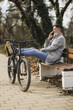 Man Resting on Park Bench Next to Bicycle Talking on Cell Phone