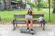 Young hipster millennial freelance woman with cool attitude, expatriate exchange student, sitting in park working online on laptop computer. Remote work, online education, e-commerce telecommuting.