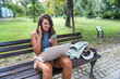 Young hipster millennial freelance woman with cool attitude, expatriate exchange student, sitting in park working online on laptop computer. Remote work, online education, e-commerce telecommuting.