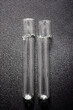 Two broken glass test tubes on a black surface