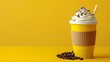   A yellow backdrop holds a cup of coffee topped with whipped cream, coffee beans, and a protruding straw