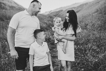 Family spending time together outdoors. A happy mother holding baby daughter, father, son walk at sunset. Children with parents happiness walking in grass in field. Black white photo in mountains