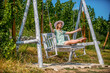 Happy girl swinging on swing. Pretty blond swinging in park on a sunny day. Attractive blonde beauty on a swing in a park. Young woman is swinging on a swing in summer park garden