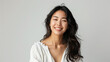 © MariКа - Portrait of a 30 year old Japanese woman smiling slightly on a grey background. Asian woman with a gentle smile and loose long hair in white shirt