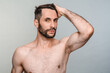 Masculinity concept. Naked handsome young man touching his hair isolated over grey background. Shirtless sexy model looking at camera, taking care of his appearance beauty