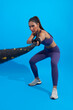 Athlete asian sportswoman waving the ropes as part of fat burning workout in fitness studio background. Woman exercising with battling ropes at the gym.