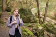 Happy young 30s woman talk phone, listen and walking in forest. Phone Communication. Young female with backpack hiking on the road in nature. Beautiful woman walking on nature in sport clothes.
