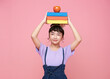 smiling young Asian girl or elementary school girl holding books on her head isolated on pink background.