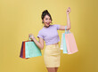 Happy pretty Asian woman carrying colorful shopping bags isolated on yellow studio background.