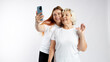 Happy older Mother and adult daughter are doing Selfie on white background. Studio shot of well-dressed female friends. Two women together doing selfie shot on mobile cell phone. Family day concept.
