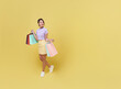Happy pretty Asian woman carrying colorful shopping bags walking to supermarket isolated on yellow copy space background.