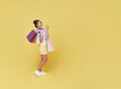 Happy pretty Asian woman carrying colorful shopping bags looking and pointing finger isolated on yellow studio copy space background.