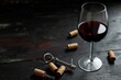 A glass of red wine is on a table with a corkscrew and a bunch of corks