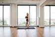 © sofiko14 - Fit young woman takes break during an intense workout in spacious modern gym with large windows overlooking city. Sports woman stands on yoga mat, demonstrating commitment to fitness and health.