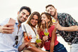 Group of four young adults taking a selfie while enjoying colorful summer cocktails outdoors - vibrant social moment - alcohol and vacation lifestyle