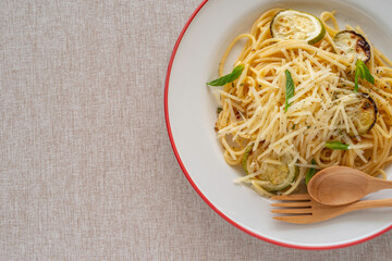 Wall Mural - Spaghetti with grilled zucchini, parmesan cheese, spices on ceramic plate over cotton fabric background.