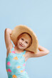 A young girl wearing a straw hat and a blue and pink swimsuit. She is smiling and looking at the camera