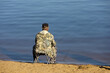 Fisherman sitting near the water with a fishing rod, rear view. Man angling on river coast at spring