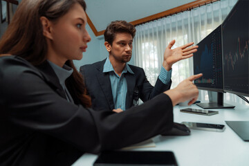 Two business traders consulting dynamic stock market in currency rate investment trading on two computer screens, woman coworker taking note with compare real time graph at modern office. Postulate.