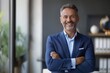 © Adriana - Happy middle aged business man ceo standing in office arms crossed. Smiling mature confident professional executive manager, proud lawyer, businessman leader wearing blue suit