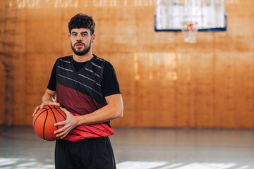 Wall Mural - Male basketball player with a ball in his hands on a sports court in a hall