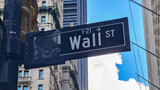 Fototapeta  - A close up on the sign, which points to the  Wall Street in New York City. There are tall buildings in the back. Famous landmarks. The sign has also a miniature of building along that street.