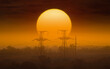 Silhouette of power transmission towers against background of huge sun