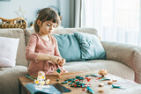 Fototapeta  - A charming little girl using small colorful construction pieces on a wooden table to craft flowers