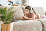 Fototapeta  - A cute little girl, watching a laptop screen, fully absorbed in her digital world. Concept: technology-infused relaxation, online education, technological entertainment