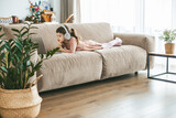 Fototapeta  - A little girl, lying on a sofa, captivated by the laptop screen in front of her, lost in her digital adventure. Concept: technology-infused relaxation, online education, technological entertainment