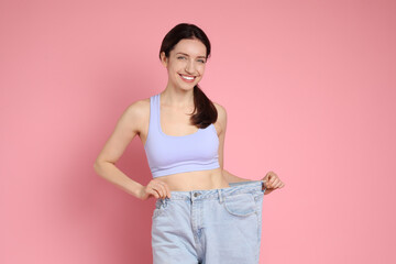 Canvas Print - Happy young woman in big jeans showing her slim body on pink background