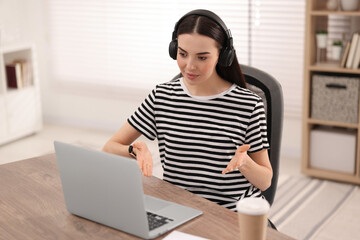 Poster - Young woman in headphones using video chat during webinar at table in room