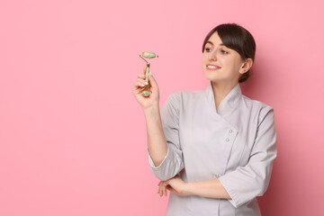 Wall Mural - Cosmetologist with facial roller on pink background, space for text