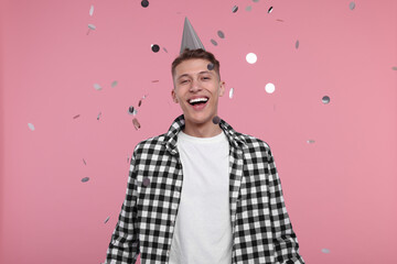 Poster - Happy man in party hat under falling confetti on pink background